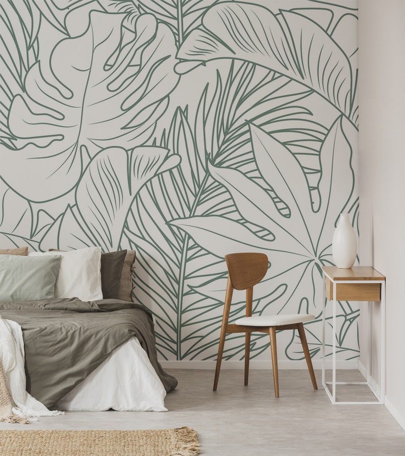 Puede incluir: Un dormitorio con una pared blanca con un dibujo de hojas tropicales en l&iacute;neas verdes. En primer plano hay una cama con un edred&oacute;n marr&oacute;n y almohadas blancas. En la esquina de la habitaci&oacute;n hay una silla de madera con un coj&iacute;n blanco. Una peque&ntilde;a mesa de madera con un jarr&oacute;n blanco est&aacute; al lado de la silla.