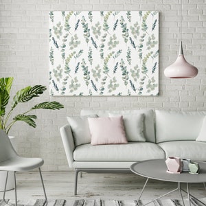 Puede incluir: Una impresión en lienzo blanco con un patrón repetitivo de hojas de acuarela verde y azul. La impresión está colgada en una pared de ladrillo blanco sobre un sofá blanco con un cojín rosa.