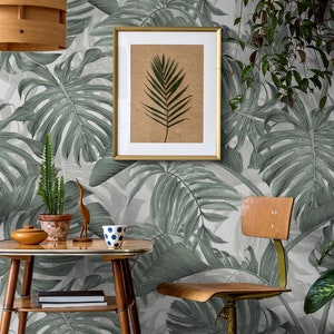 May include: A gray and white tropical leaf patterned wallpaper with a framed print of a single green leaf, a wooden table with a potted cactus, a wooden bird sculpture, a mug, and a chair.