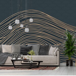 May include: A living room interior design with a dark blue wall featuring a gold abstract line pattern wallpaper. A light grey sofa with throw pillows and a blanket sits in front of the wall. A coffee table with a vase of greenery and a book sits in front of the sofa. A potted plant sits on the right side of the image.