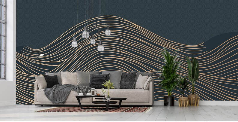 May include: A living room interior design with a dark blue wall featuring a gold abstract line pattern wallpaper. A light grey sofa with throw pillows and a blanket sits in front of the wall. A coffee table with a vase of greenery and a book sits in front of the sofa. A potted plant sits on the right side of the image.