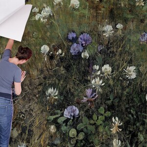 May include: A person is applying a floral wallpaper with a green background and white and purple flowers. The wallpaper has a textured, painterly look.