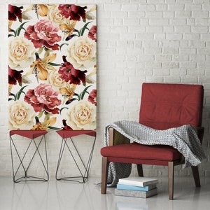 Puede incluir: Un lienzo floral con rosas y lirios crema, burdeos y melocotón. Dos mesas auxiliares rojas con patas de metal negro están frente a la impresión. Una silla roja con una manta y libros está a la derecha.
