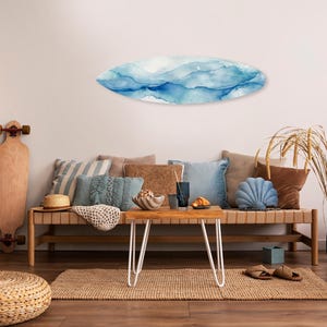 May include: A living room scene with a surfboard-shaped wall art featuring blue watercolor waves. A long wooden bench holds pillows in various shades of blue and brown. A skateboard and a woven ottoman are also present.