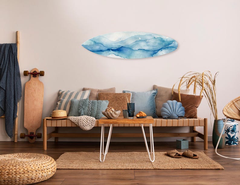 May include: A living room scene with a surfboard-shaped wall art featuring blue watercolor waves. A long wooden bench holds pillows in various shades of blue and brown. A skateboard and a woven ottoman are also present.