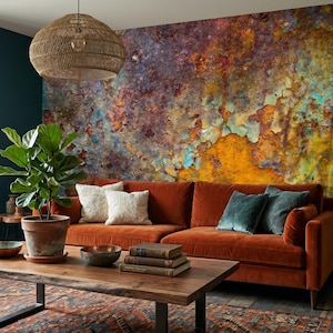 Könnte beinhalten: Ein Wohnzimmer mit einer großen Akzentwand, die mit einem strukturierten Wandbild in Rostoptik in Orange-, Türkis- und Dunkellila-Tönen gestaltet ist. Ein Sofa aus rostorangem Samt steht vor der Wand, ergänzt durch einen Holztisch und eine Pflanze.