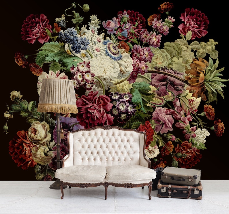May include: A white tufted sofa with wooden legs sits in front of a dark background with a large floral arrangement of red, pink, and white flowers.