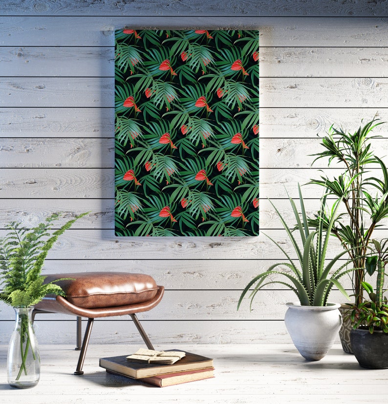 Puede incluir: Una impresi&oacute;n enmarcada de un patr&oacute;n de hojas tropicales con flores rojas sobre un fondo verde oscuro. La impresi&oacute;n est&aacute; colgada en una pared de madera blanca con un otomano de cuero marr&oacute;n y plantas en macetas delante.