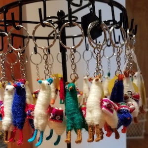 Puede incluir: Un expositor de llaveros de llama de colores hechos de hilo. Las llamas son de varios colores, incluyendo blanco, azul, verde y rojo. Los llaveros están colgados de un estante de metal.