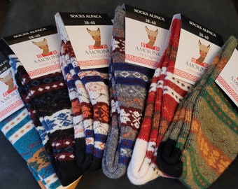 May include: Five pairs of colorful alpaca socks with geometric patterns. The socks are folded and arranged in a semi-circle. Each sock has a tag attached with the words "Socks Alpaca" and "Amorink Peru Alpaca" printed on it.