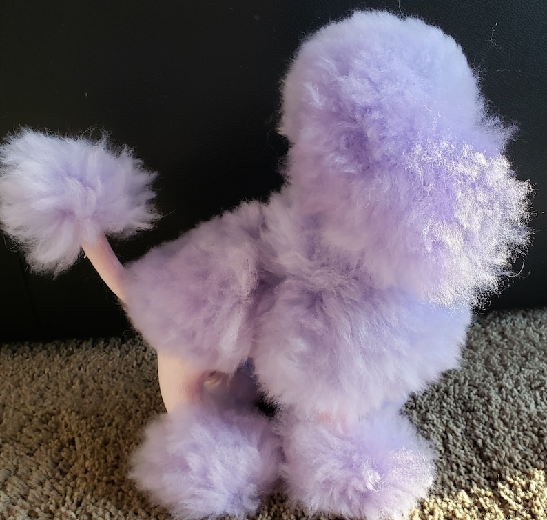K&ouml;nnte beinhalten: Ein Pl&uuml;sch-Pudel-Spielzeug in Lavendel mit einem flauschigen Schwanz und einer rosa Nase.