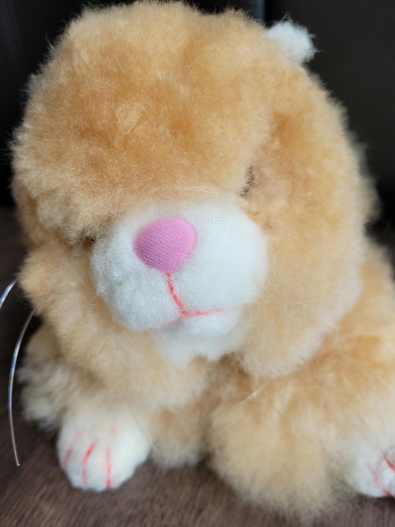 May include: A plush toy in the shape of a brown and white bunny with pink nose and red claws. The bunny is sitting with its head tilted to the side.