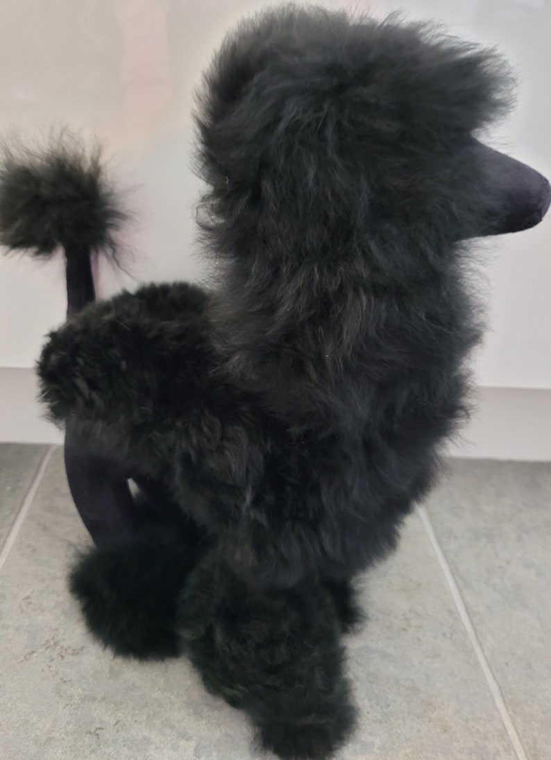 K&ouml;nnte beinhalten: Ein schwarzes Pl&uuml;sch-Pudel-Spielzeug mit einem flauschigen Fell. Das Spielzeug steht auf seinen Hinterbeinen mit seinem Schwanz eingerollt.