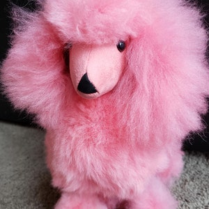 K&ouml;nnte beinhalten: Ein flauschiges rosa Pl&uuml;schtier in Form eines Pudels. Das Spielzeug hat eine schwarze Nase und rosa Augen.