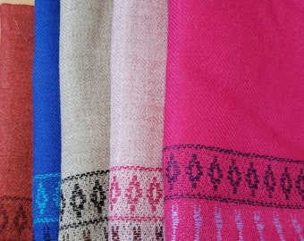 May include: A collection of colorful scarves in shades of red, blue, beige, pink, and fuchsia. Each scarf features a patterned border with geometric designs. The scarves are folded and stacked, showcasing their textures and colors.