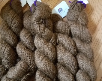 Könnte beinhalten: Drei Knäuel braunes Garn mit violetten Etiketten. Das Garn hat eine weiche, flauschige Textur.