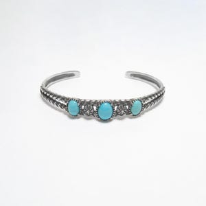 May include: A silver bangle bracelet with three turquoise stones set in a floral design.