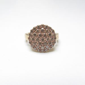 Op de afbeelding: Een gouden ring met een ronde cluster van kleine bruine en witte diamanten.