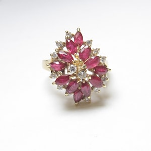 Op de afbeelding: Een gouden ring met een bloemmotief, bezet met marquise-geslepen robijnen en kleine diamanten. De robijnen hebben een dieprode kleur en zijn gerangschikt in een bloemachtig patroon. De diamanten zijn helder en sprankelend.