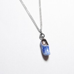 May include: A silver chain necklace with a blue and white ceramic clog pendant. The clog has a blue and white design and the word "Het" written on it.