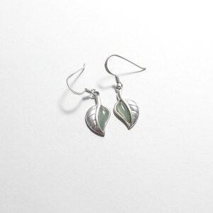 May include: A pair of silver earrings with a green stone leaf design.