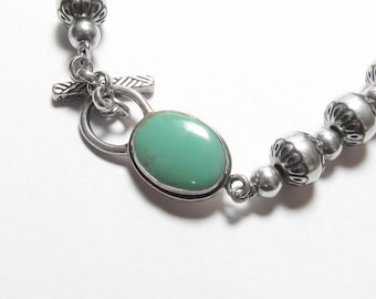 May include: A silver bracelet with a turquoise stone and a toggle clasp. The bracelet is made of round beads with a decorative design.