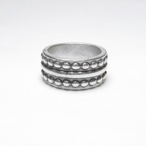 May include: A silver ring with a textured design. The ring features two rows of small, raised beads separated by a smooth band. The ring is a simple, yet elegant piece of jewelry.
