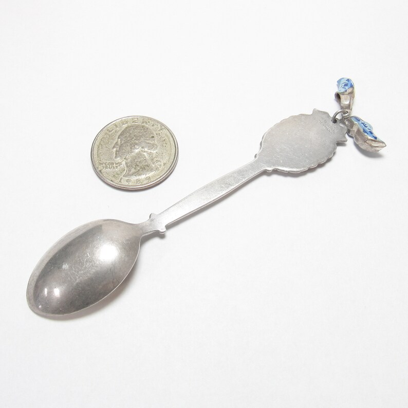 Pode incluir: Colher de prata com um amuleto de esmalte azul e branco. A colher &eacute; do tamanho de uma moeda de 25 centavos.