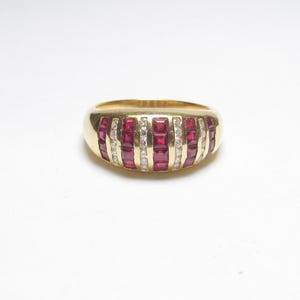 May include: A gold band ring featuring a channel setting with alternating vertical rows of square-cut red rubies and round-cut clear diamonds. The polished yellow gold metal creates a smooth, rounded profile across the top of the finger.