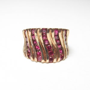 May include: A gold ring with a wavy design set with red gemstones.