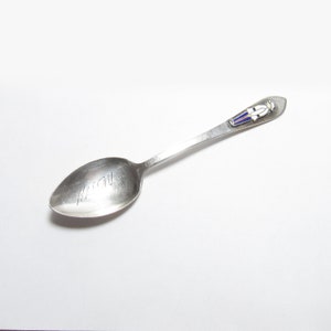 May include: A silver teaspoon with a blue and white enamel figure of a soldier on the handle. The spoon has the word "Nathan" engraved on the bowl.