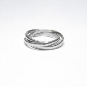 May include: A silver-colored ring with three interlocking bands. The bands are smooth and rounded, creating a continuous, flowing design. The ring is set against a plain white background, highlighting its simple elegance.