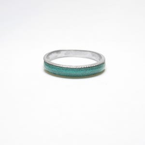 May include: A silver ring with a band of teal enamel. The ring has a textured border and a smooth, polished finish. The ring is a simple, elegant piece of jewelry.