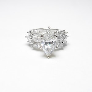 May include: A silver ring featuring a large marquise-shaped diamond surrounded by smaller marquise-shaped diamonds.
