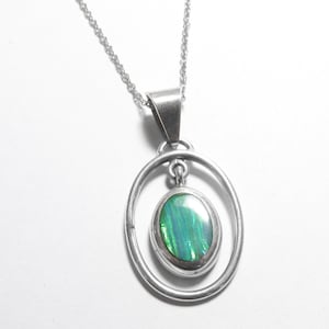 May include: A silver pendant necklace featuring an oval-shaped green iridescent stone set within a smooth silver oval frame. The pendant hangs from a delicate silver chain, showcasing a polished metallic finish and a vibrant, multi-tonal green center.