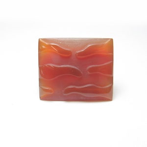 May include: A square, orange-red carnelian gemstone with a carved, wavy pattern.