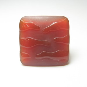May include: A square, red glass ring with a wavy, textured design.
