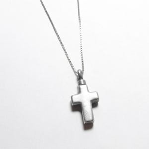 以下が含まれることがあります： 銀色のチェーンネックレスに銀色の十字架のペンダントが付いている。