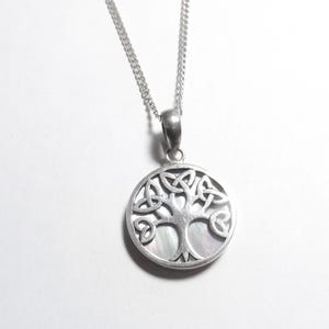 May include: Silver-tone pendant necklace featuring a circular pendant with a Celtic tree of life design. The pendant has a mother-of-pearl background and hangs from a delicate chain. The tree design is intricately detailed.