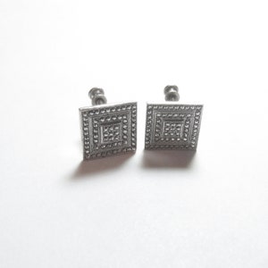 May include: A pair of silver square earrings with a textured design.