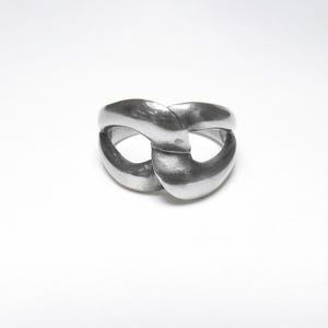 May include: A silver-toned ring with a unique, intertwined design. The ring features two interlocking, oval-shaped bands that create a figure-eight appearance. The metal has a smooth, polished finish, reflecting light and adding a touch of elegance to the jewelry.