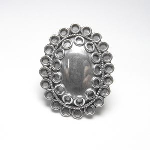 May include: A silver ring with a large oval center piece surrounded by a circle of smaller circles.