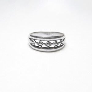 May include: A silver ring with a geometric design. The ring has a wide band with a row of diamond-shaped cutouts.