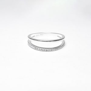 May include: A silver ring with a thin band and a row of small clear stones on the bottom band. The ring is marked "925" on the inside.