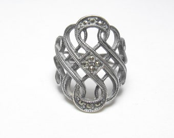 May include: A silver ring with a delicate, intricate design featuring a woven knot pattern accented with small, sparkling marcasite stones.