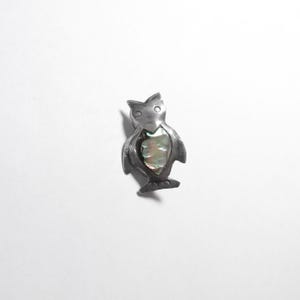 May include: A silver-coloured owl brooch featuring an abalone shell inlay. The brooch has a detailed design with visible wings, feet, and eyes. The abalone shell has iridescent colours of green, blue, and purple.