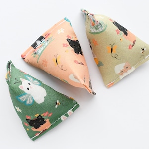 May include: Three catnip-filled cat toys in a triangular shape. The toys are decorated with floral and cat patterns in shades of green, peach, and tan. Each toy has a small loop at the top.