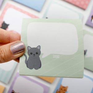 May include: A light green sticky note with a gray cartoon cat illustration and a white speech bubble. The note is held in a hand, with other cat-themed notes in the background. The text "Chester & Print" is visible.