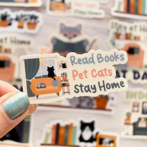 K&ouml;nnte beinhalten: Ein Aufkleber mit dem Text "Read Books, Pet Cats, Stay Home" und einer Katzen-Illustration. Die Illustration zeigt eine Katze auf einem Sofa, ein Fenster und einen kleinen Beistelltisch mit Pflanzen.