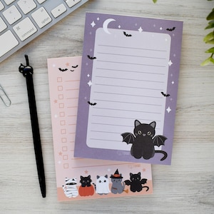 May include: A set of Halloween-themed stationery featuring a black cat with bat wings, bats, and a crescent moon. Includes a lined notepad, a to-do list notepad, and a black cat pen. The stationery is decorated with bats and stars.